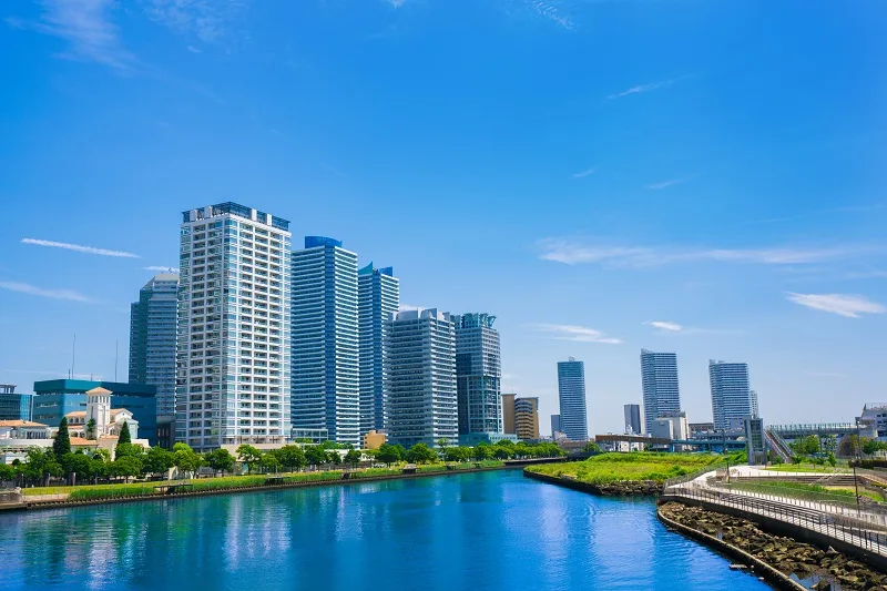 青空の下、水辺沿いに並び立つ高層マンション群の外観写真(マンション管理組合の火災保険をイメージした画像)